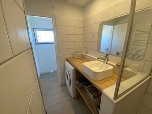 A compact bathroom with a built-in washing machine, a white sink, and a mirror above it.