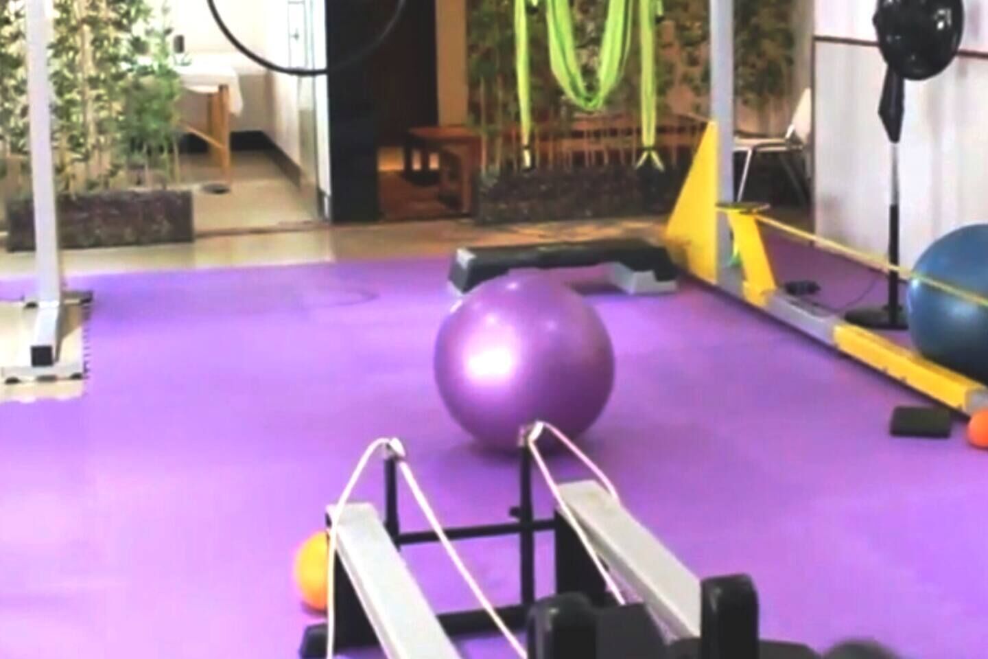 Una pelota de ejercicios morada sobre un suelo morado, con equipo de gimnasio al fondo.