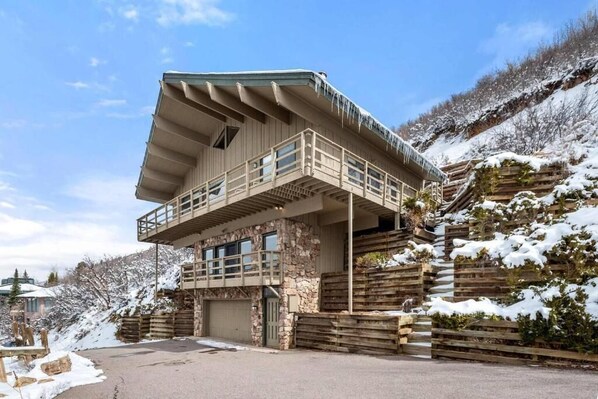 A two-story log cabin with a balcony, stone foundation, and a garage.