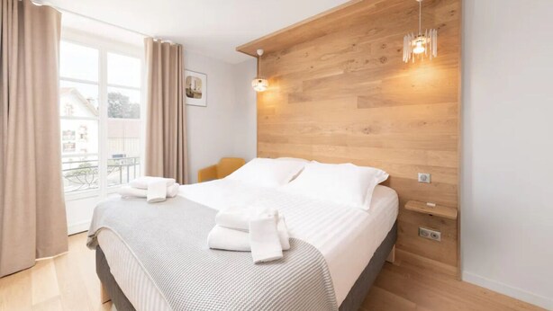 Une chambre d’hôtel moderne avec un grand lit, une tête de lit en bois et un balcon avec vue.