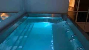 Un bain à remous rectangulaire avec un éclairage bleu, entouré de murs et doté d’une fenêtre.