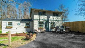 A two-story house with a patio area, a small attached garage, and a wooden fence. - Hadley Hideaway Cottage (Hadley)