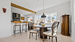 Un coin repas comprenant une table ronde, quatre chaises, un grand meuble en bois et une suspension.