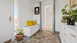 Un couloir avec un banc, une plante en pot, un tableau encadré et un escalier menant à une autre pièce.