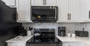 Una cocina moderna con gabinetes blancos, un microondas negro, una estufa de acero inoxidable y una cafetera.
