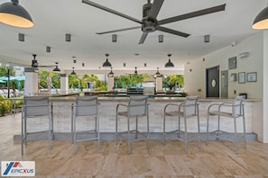 A modern bar area with a ceiling fan, multiple pendant lights, and bar stools.
