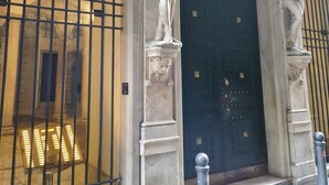 Ein Gebäudeeingang mit einer dunkelblauen Tür, gesäumt von klassischen Statuen und aufwendigen architektonischen Details.