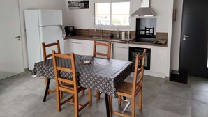 A compact kitchen with a dining table, chairs, a refrigerator, a stove, and a window. - Gite DU Vieux Chene (Reignac)