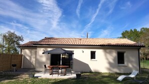 A single-story house with a tiled roof, a patio with a table and chairs, and a covered outdoor area. - Gite DU Vieux Chene (Reignac)