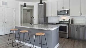 A modern kitchen with a central island, bar stools, a microwave, and an oven.