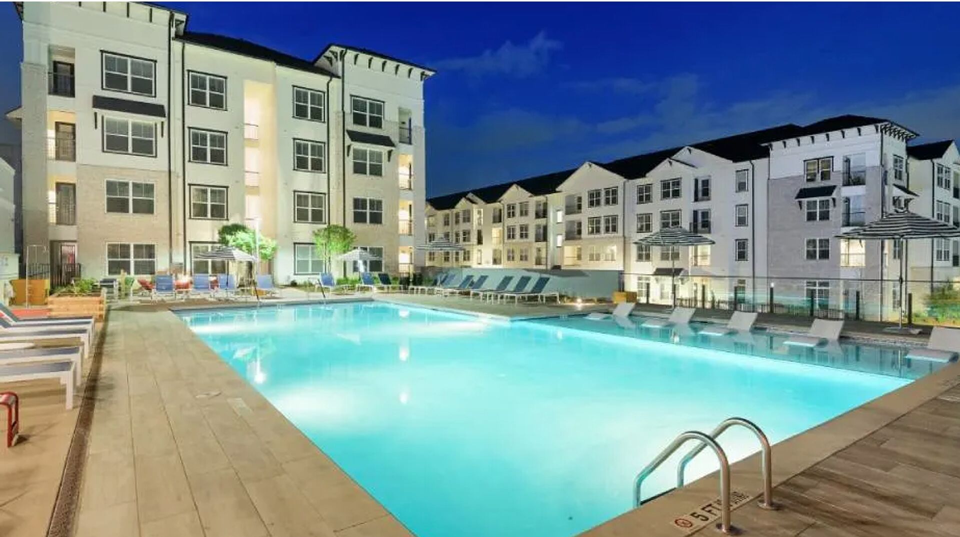Ein Hotel mit Schwimmbad, mehreren Balkonen und einer gut beleuchteten Außenansicht im Abenddämmerung.