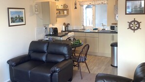 A compact living space with a dining area, kitchen, and a black leather sofa. - Cosy and comfortable Riverside Cottage in Wroxham, the Gateway to the Broads (Wroxham)