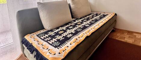 Un lit simple avec une couverture à motifs, une chaise et une fenêtre ornée de rideaux légers.