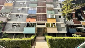 Un immeuble résidentiel à plusieurs étages, doté de balcons, d’une entrée principale et d’un petit jardin.