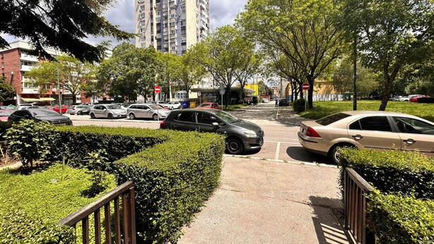 Une rue de la ville, avec des voitures garées, un chemin piétonnier et de grands immeubles en arrière-plan.