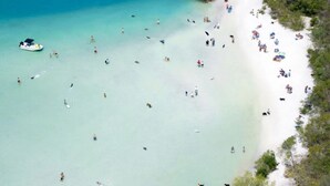 An aerial view of a beach with clear turquoise waters, a boat, and people on the shore. - Custom Pool! Tiki Bar | Private Yard ~ Enjoy SWFL (Fort Myers)