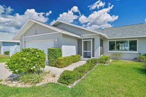 A modern single-story house with a garage, a covered entryway, and a well-maintained front yard with shrubs and a small tree. - Custom Pool! Tiki Bar | Private Yard ~ Enjoy SWFL (Fort Myers)