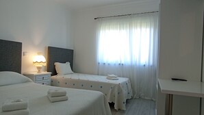 A hotel room with two beds, a desk, a TV, and a window with curtains. - Casa Talika (Ourem)