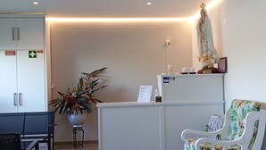 A reception area with a desk, a chair, a potted plant, and a statue on a shelf. - Casa Talika (Ourem)