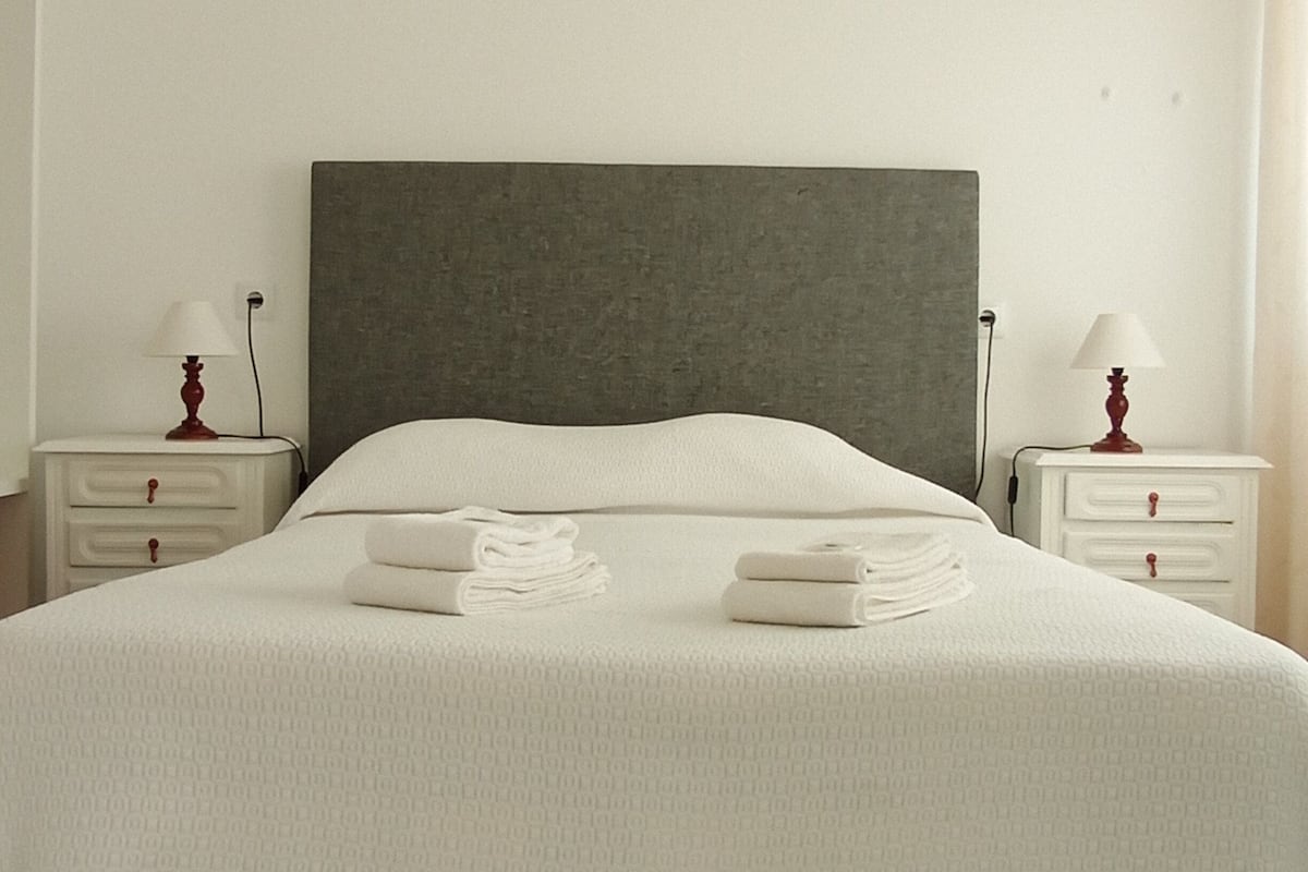 A neatly made bed with a grey headboard, white bedding, and two bedside tables with lamps.