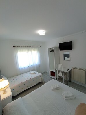 Een kleine, schone kamer met een bed, een bureau, een stoel, een televisie en een radiator.