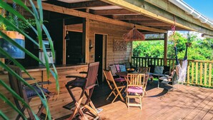 Una terraza de madera con mobiliario exterior, una lámpara colgante y vistas a zonas verdes.