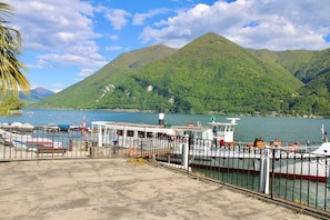 Eine Fähre an einem Anleger, mit einem Boot, einer Betonplattform und einem Berg im Hintergrund.