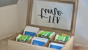 A wooden box with compartments containing Linpha tea packets, a metal latch, and a whiteboard with handwritten text. - The Painter's Nest + Lake Garden (Cima)