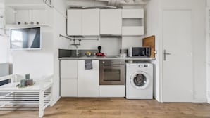 A compact kitchen with white cabinetry, a washing machine, a microwave, and a small countertop with various items.