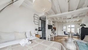 A spacious bedroom with a large bed, a desk, and a view of the kitchen and living area.