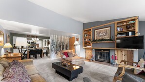 A modern living room with a sofa, armchair, and coffee table. There is a fireplace, a television, and a bookshelf.