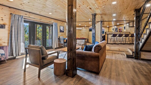 Un interior acogedor de cabaña con techo de madera, un sofá, una silla y un comedor con barra.