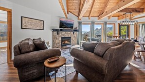 Un salón acogedor con chimenea de piedra, vigas de madera y un amplio ventanal con vistas a un paisaje pintoresco.
