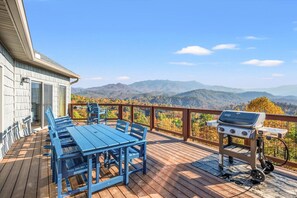Una terraza con una mesa y sillas azules, una parrilla y una vista panorámica a las montañas.