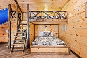 Una cabaña de madera con cama en un altillo, escalera y un tobogán azul.