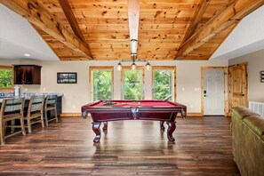 Une pièce spacieuse avec une table de billard, des poutres en bois au plafond et de grandes fenêtres.