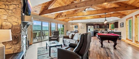 A spacious living room with a pool table, leather chairs, and a stone wall.