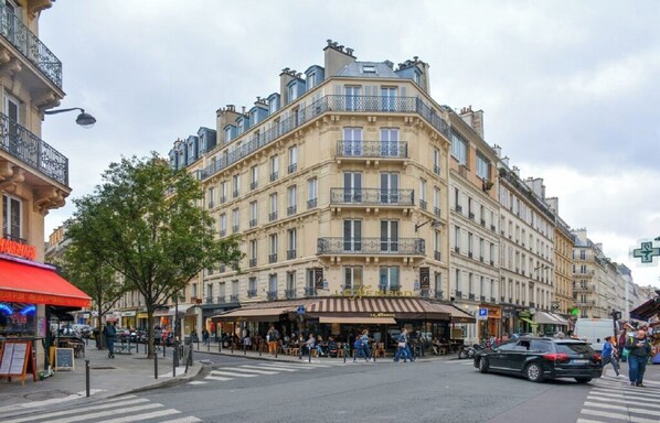 A multi-story building with a café on the ground floor, a visible restaurant, and a street intersection with pedestrians and vehicles.