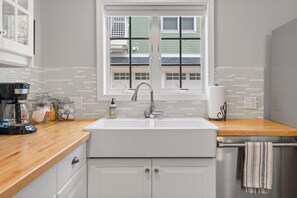A kitchen with a white sink, a coffee maker, and a window with blinds. - La Maison on Main with views of the Harbor Point and a Private Courtyard! (Harbor Springs)