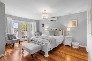 Un dormitorio con cama, mesitas de noche, una silla, una ventana y una puerta.