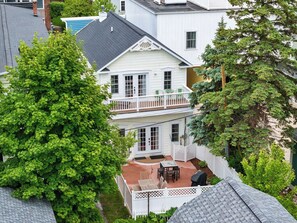 Una casa de dos pisos con balcón, un patio con mobiliario exterior y un jardín bien cuidado.