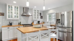 Una cocina moderna con armarios blancos, una estufa de acero inoxidable y una isla grande con dos sillas blancas.