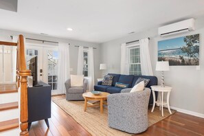 A living room with a blue sofa, two armchairs, a coffee table, a TV stand, and a painting of a beach scene. - La Maison on Main with views of the Harbor Point and a Private Courtyard! (Harbor Springs)