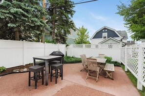 A backyard patio with a grill, dining table, and chairs. - La Maison on Main with views of the Harbor Point and a Private Courtyard! (Harbor Springs)