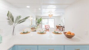 Une cuisine lumineuse avec un plan de travail blanc, des armoires bleues et un îlot central sur lequel se trouve un panier de fruits.