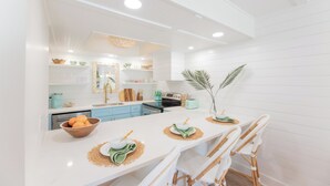 Une cuisine moderne avec des meubles blancs, un îlot central doté de sièges et un coin repas avec des chaises blanches.