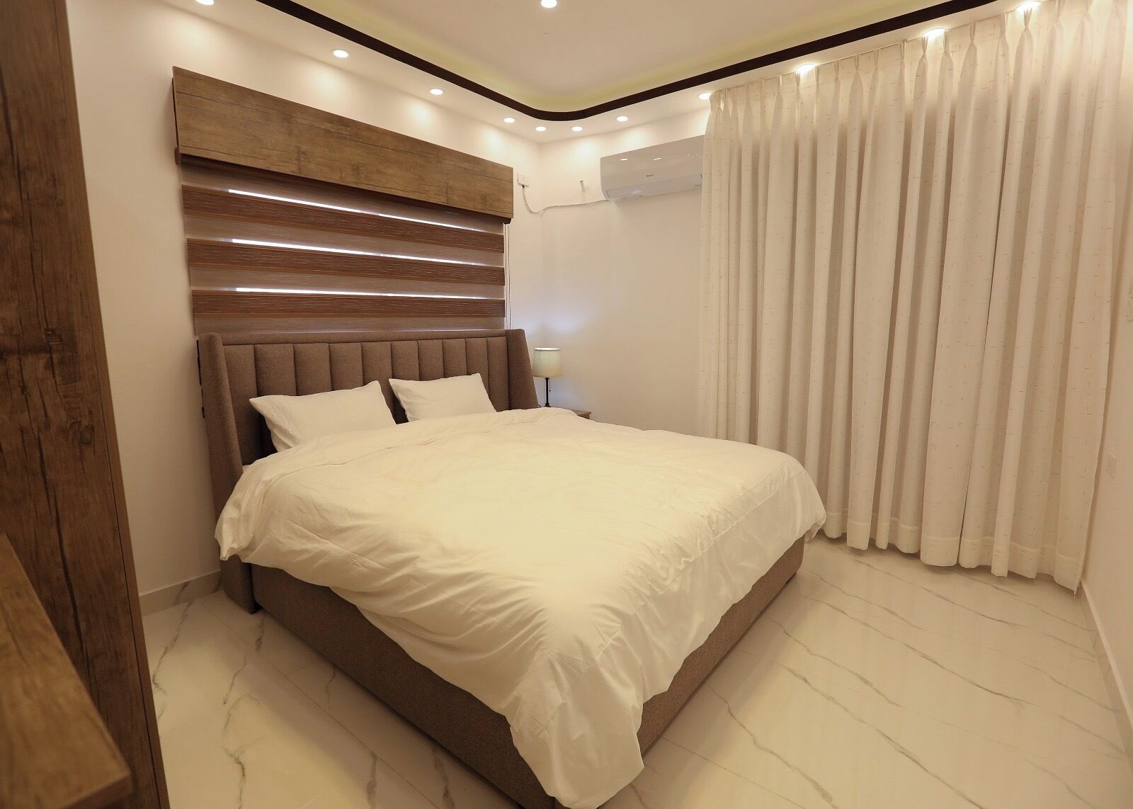 Ein modernes Schlafzimmer mit einem großen Bett, einem Holz-Kopfteil und einer Deckenleuchte.