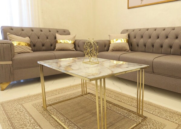 Una sala de estar con un sofá capitonado, una mesa de centro de mármol y una alfombra estampada.