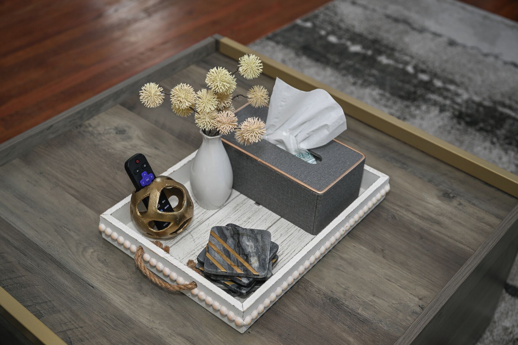 A tray with a tissue box, a vase with dried flowers, a decorative shell, and a golden spherical object.
