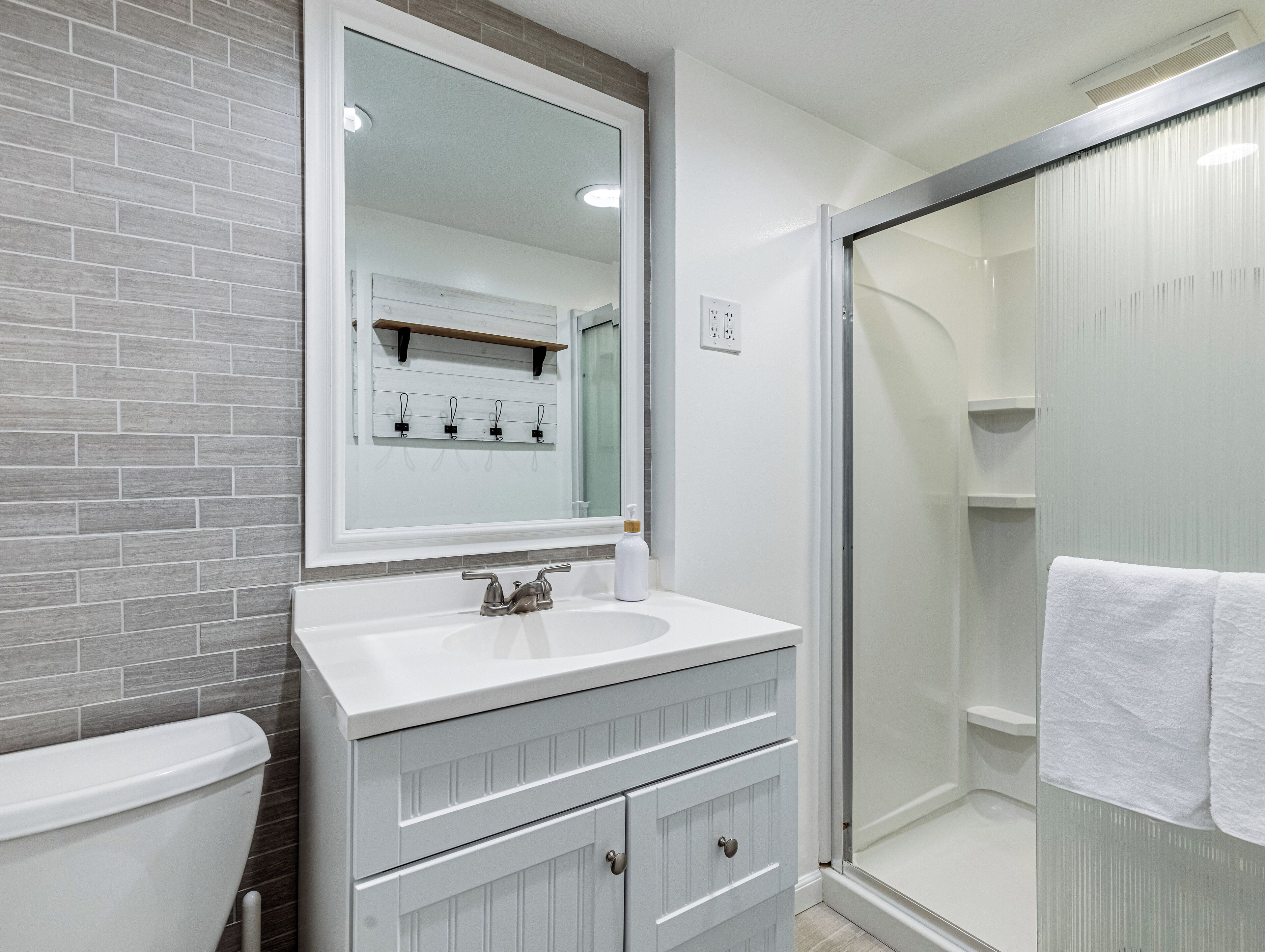 A bathroom with a white sink, a mirror, a toilet, and a shower area.